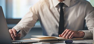 Man in a shirt and tie going over papers and working on computer
