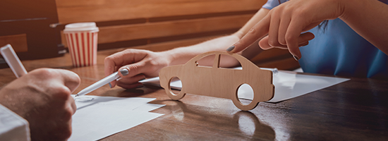 Two people sitting at desk with model car and paperwork